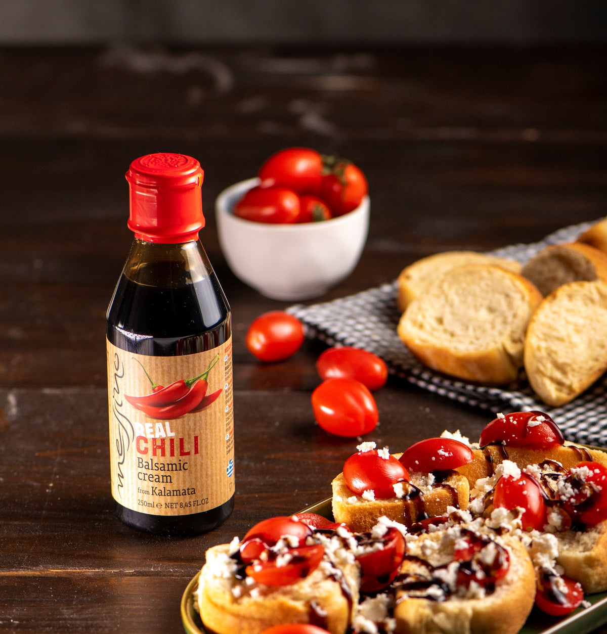 Bottle of chili balsamic cream on a wooden table with bruschetta and tomatoes.