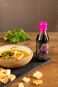 Bowl of soup with a bottle of Classic balsamic vinegar glaze on a wooden table
