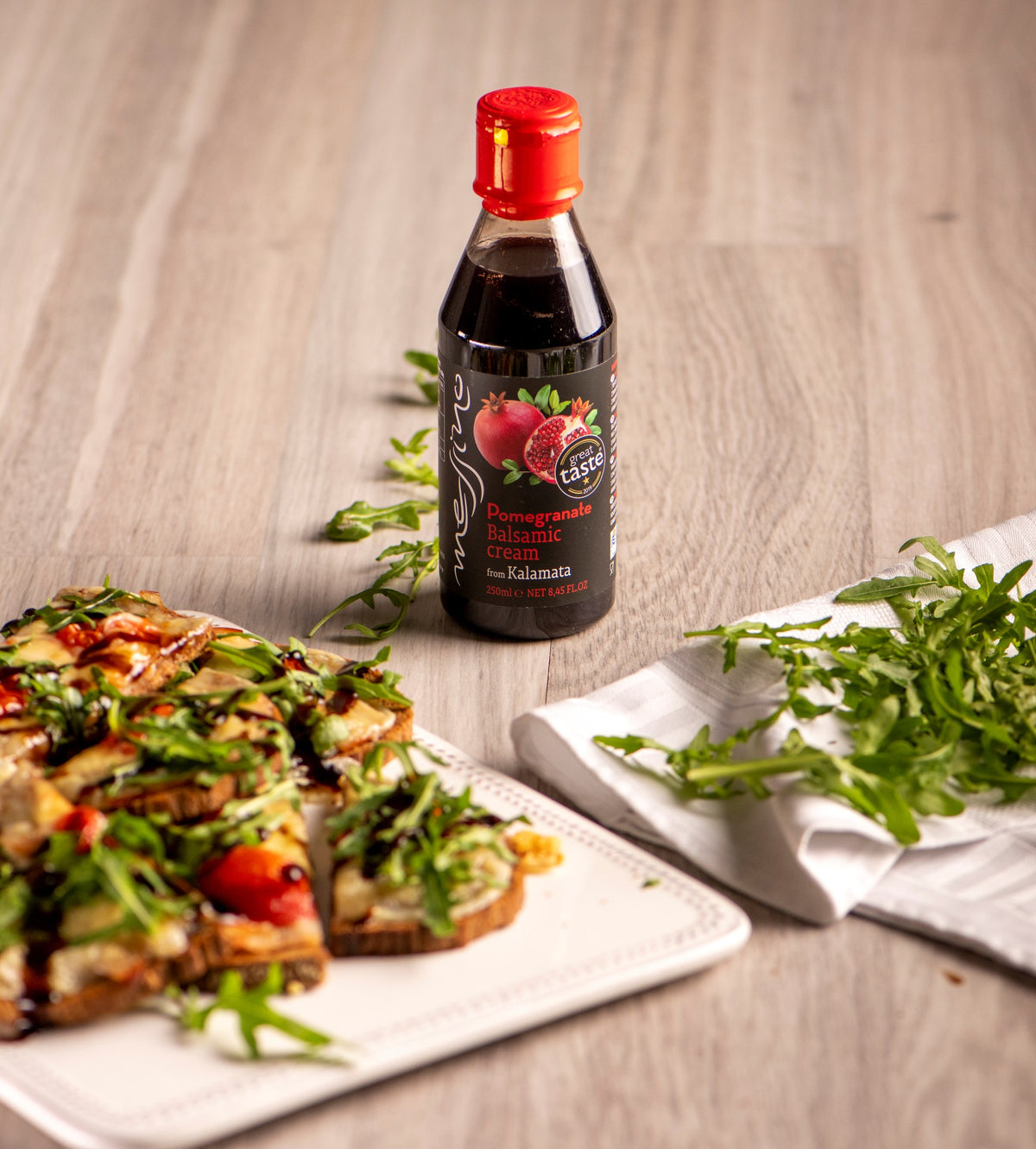 Bottle of Messino Pomegranate balsamic cream on a wooden surface with a plate of salad and bread.