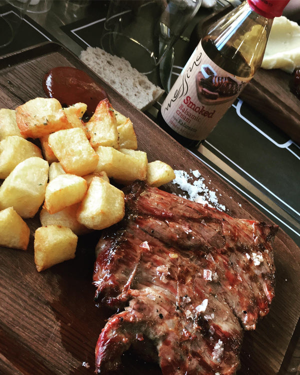Plated steak with roasted potatoes and a bottle of sauce on a wooden board.