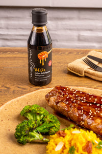 Bottle of Messino glaze on a wooden table with grilled salmon, broccoli, and yellow rice.