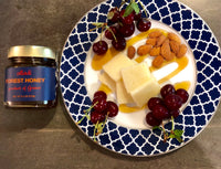 Jar of Oilladi forest honey with plate of fruits, nuts and cheese drizzled with honey 