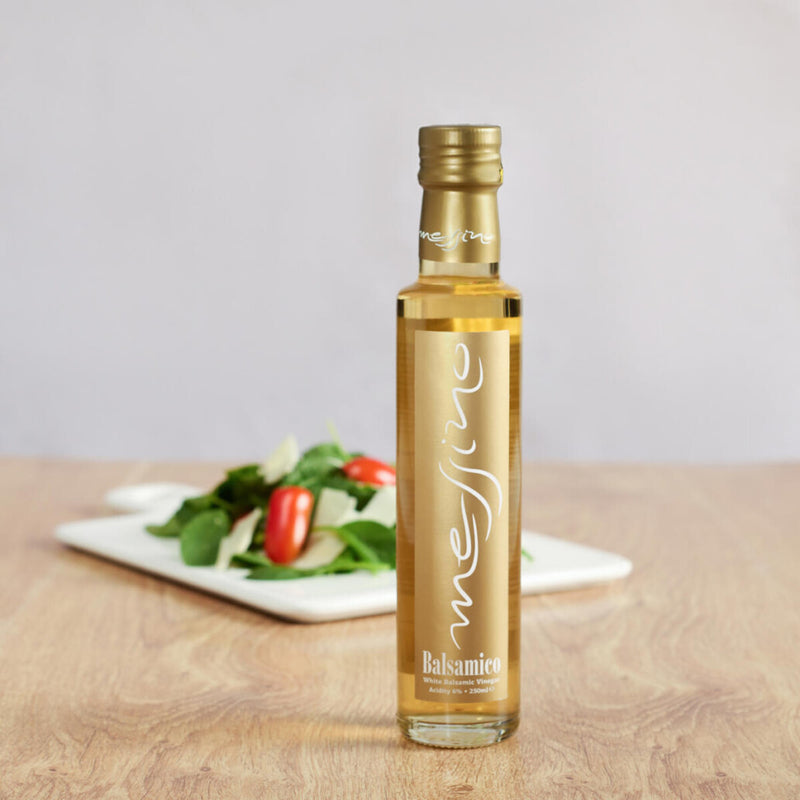 Bottle of Messino White Balsamic Vinegar with plated salad in the background