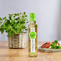 Bottle of Messino White Wine Vinegar with Oregano and plated caprese in the background with Oregano plant