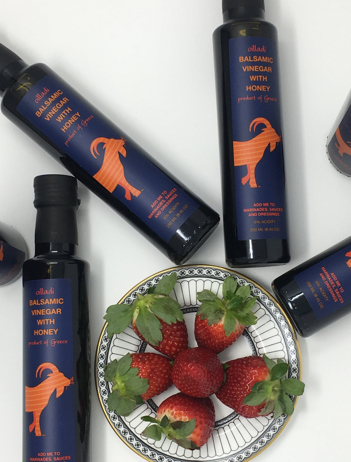 Plate of strawberries surrounded by bottles of Oilladi balsamic vinegar with honey