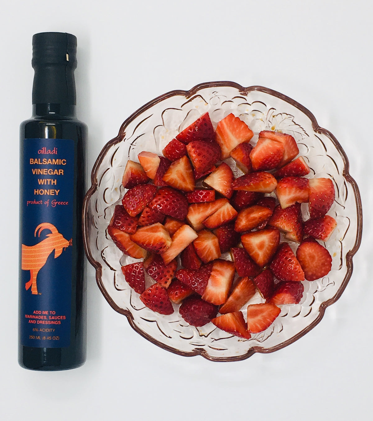 Bottle of Oilladi balsamic vinegar with honey and a plate of strawberries