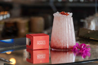 Box of Messino Pomegranate Pearls next to glass of ice topped with pomegranate pearls